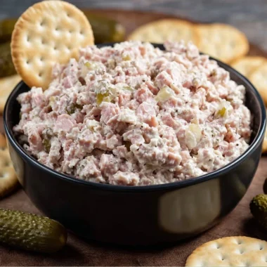 A bowl of homemade ham salad garnished with herbs and served with crackers.