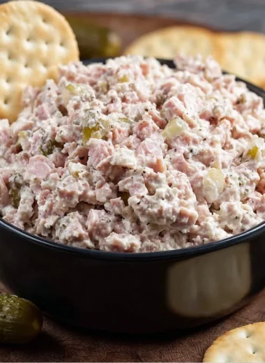 A bowl of homemade ham salad garnished with herbs and served with crackers.