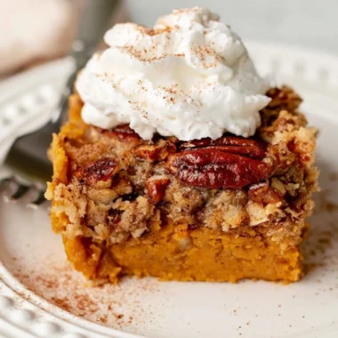 Cozy pumpkin dump cake served in a dish, topped with whipped cream.